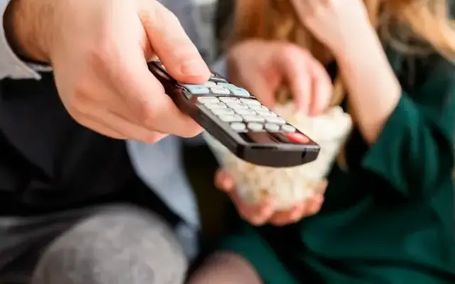 Mão segurando o controle remoto diante da TV