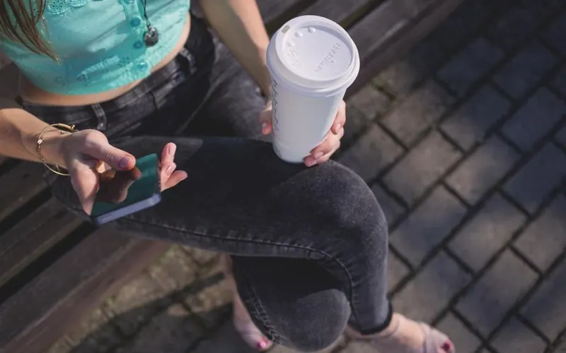 Mulher com celular e café no parque